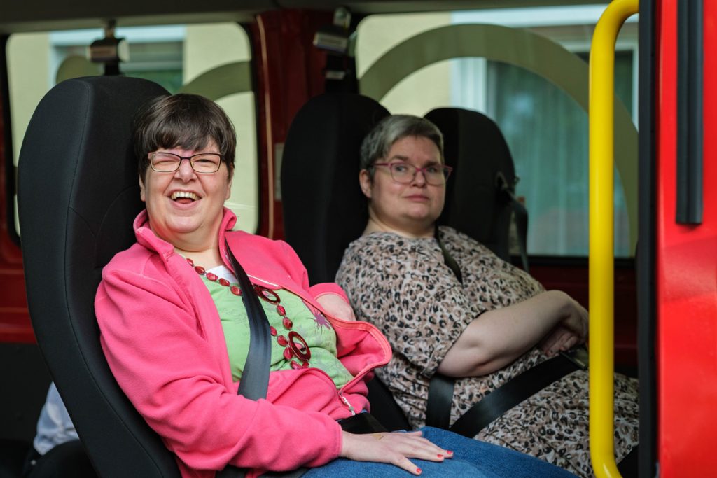 Zwei Frauen sitzen nebeneinander im Köhler-Transfer-Bus, die vordere lacht fröhlich in die Kamera.