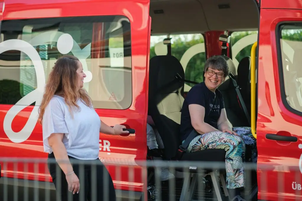 Zwei Frauen unterhalten sich lachend am roten Köhler-Transfer-Bus, die Stimmung ist gelöst.