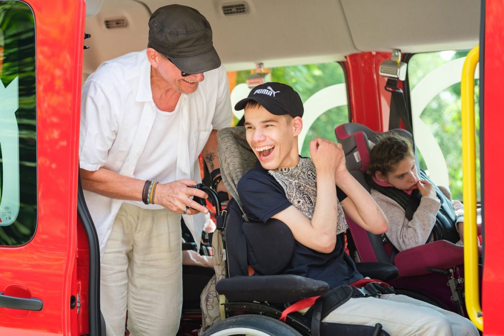 Ein junger Mann im Rollstuhl lacht herzlich, während er im Köhler-Transfer-Bus begleitet wird.