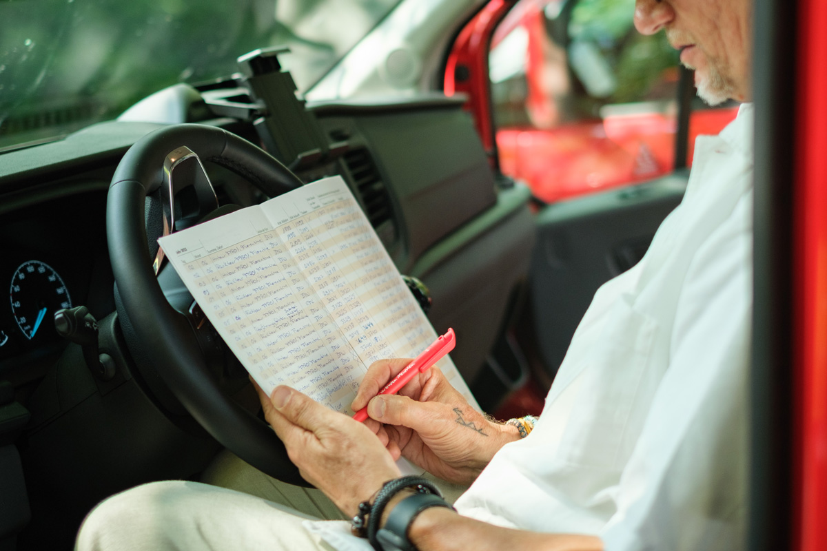 Ein Fahrer sitzt im Köhler-Transfer-Bus und trägt mit rotem Stift Daten ins Fahrtenbuch ein.